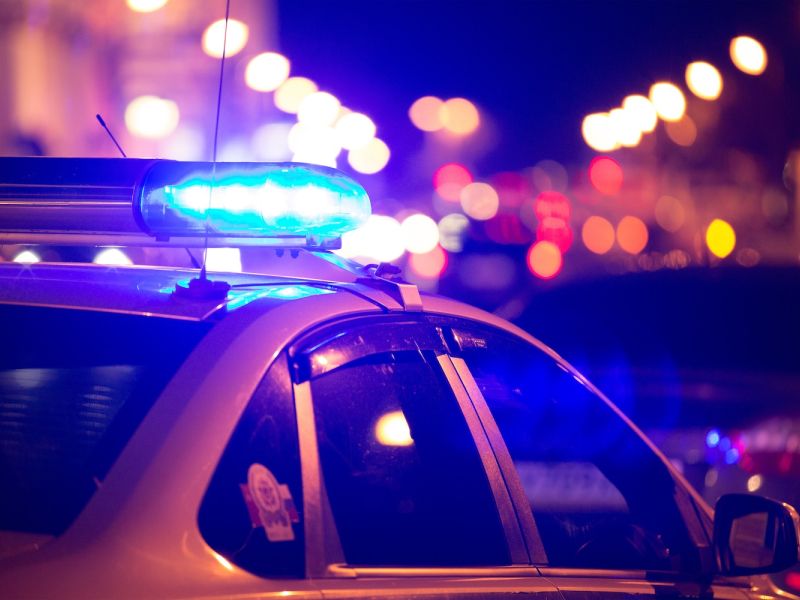 Police car with flashing blue lights at night, street in bokeh background.