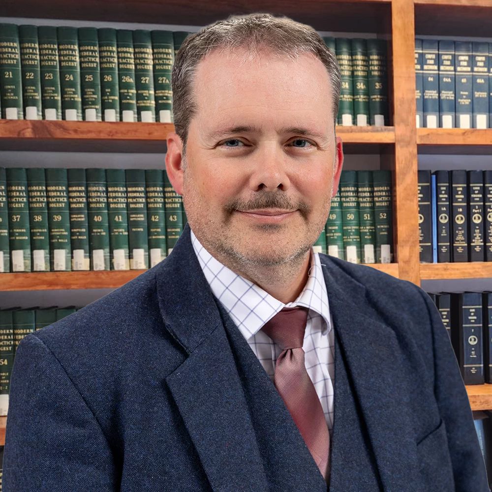 Professional man in a suit and tie standing in front of a bookshelf filled with legal books.