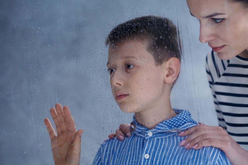 Boy and woman looking through rainy window, expressing contemplation and connection.