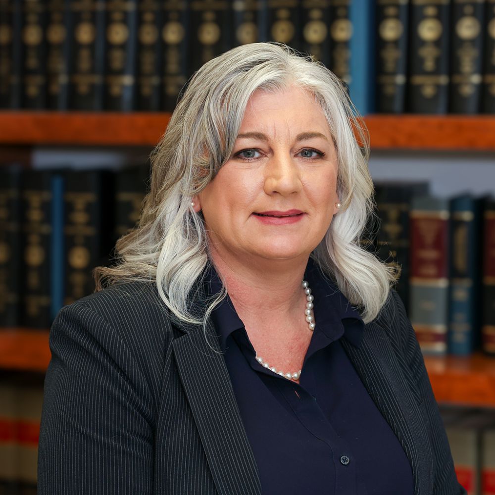 Tammy McClenney in a suit poses confidently in a library with legal books. Business, expertise, and elegance.