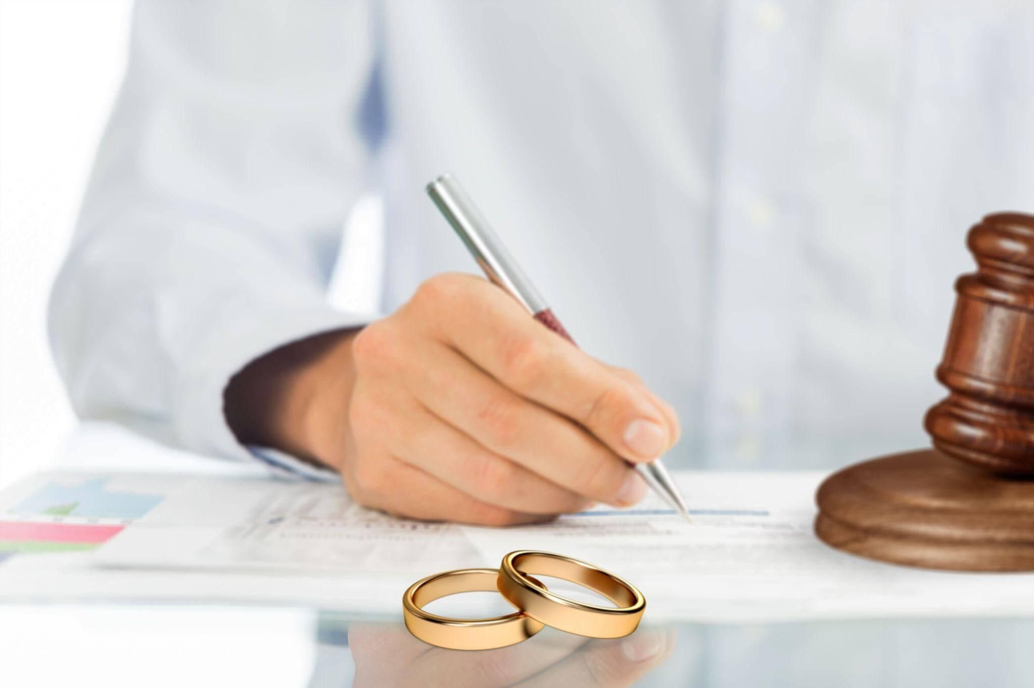 a person writing on a piece of paper with two wedding rings next to them