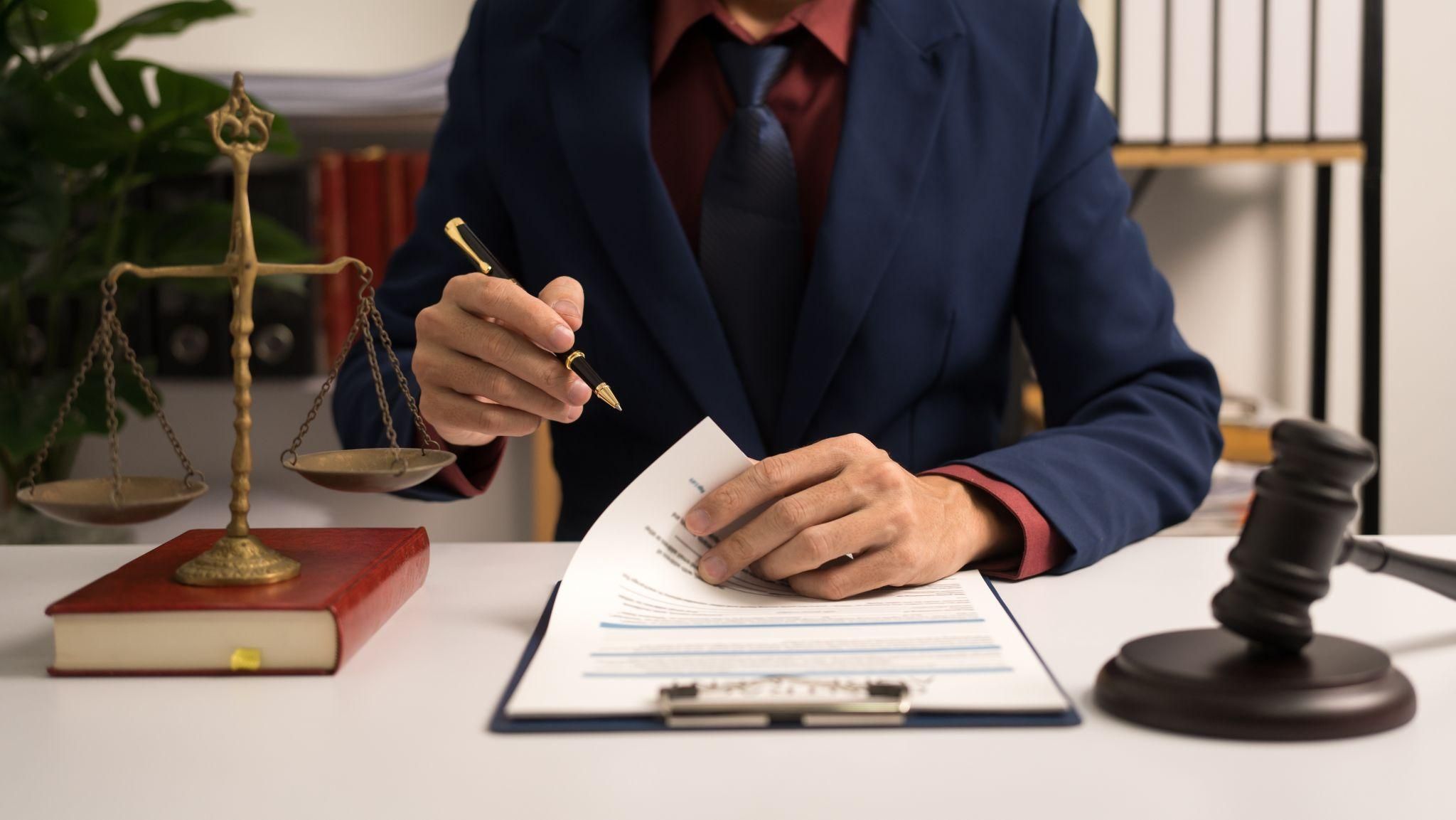 Legal professional reviewing documents at desk with scales of justice and gavel, emphasizing law and order.