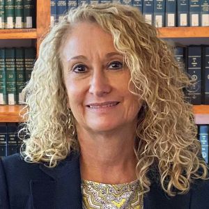 Portrait of a smiling woman with curly hair in front of bookshelves.