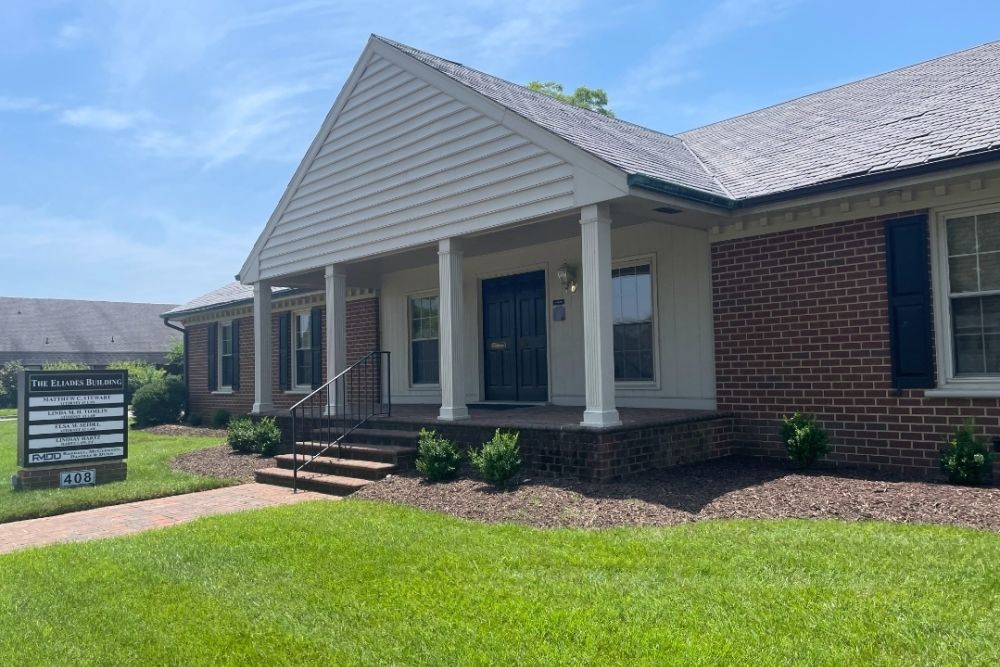Single-story brick office building with white columns and front lawn on a sunny day.