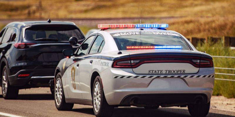 State trooper car with flashing lights pulls over a dark SUV on a rural road. Emergency response and law enforcement.