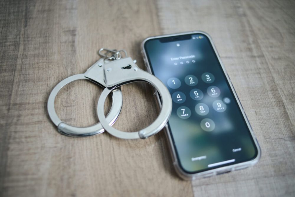 image of phone showing security password on screen and handcuffs on wooden background.