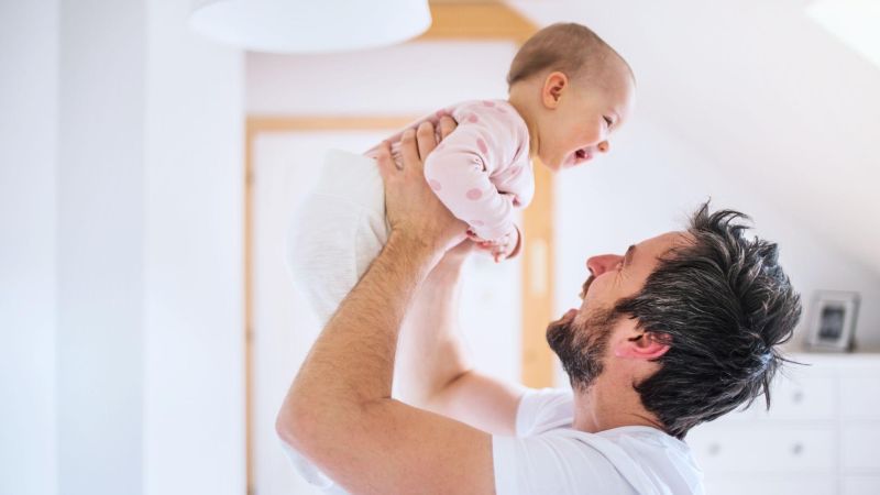 Father joyfully lifting smiling baby in bright room, showcasing parent-child bonding and happiness.