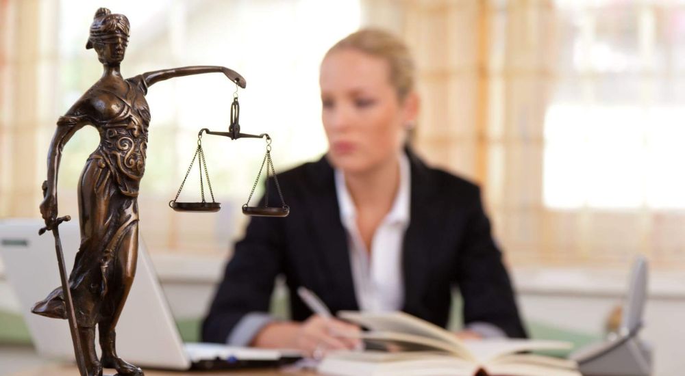 a lady sitting at a desk with a book and a statue of lady justice