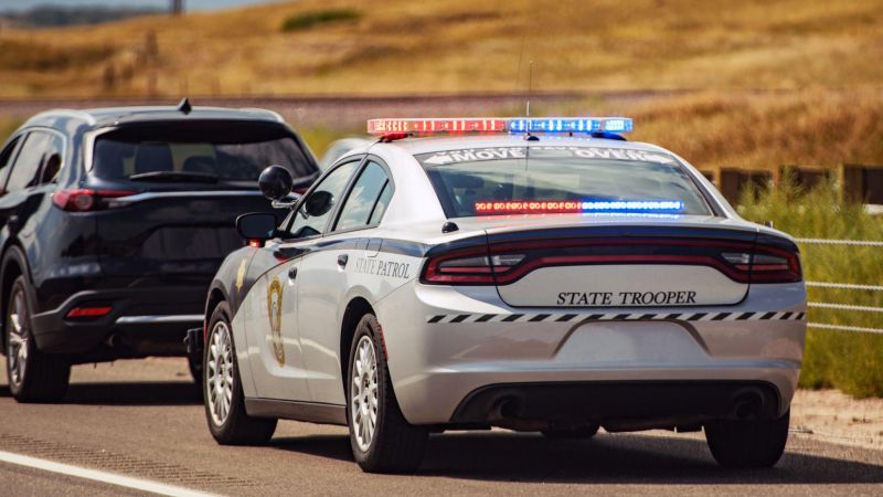 State trooper car with flashing lights pulls over a dark SUV on a rural road. Emergency response and law enforcement.