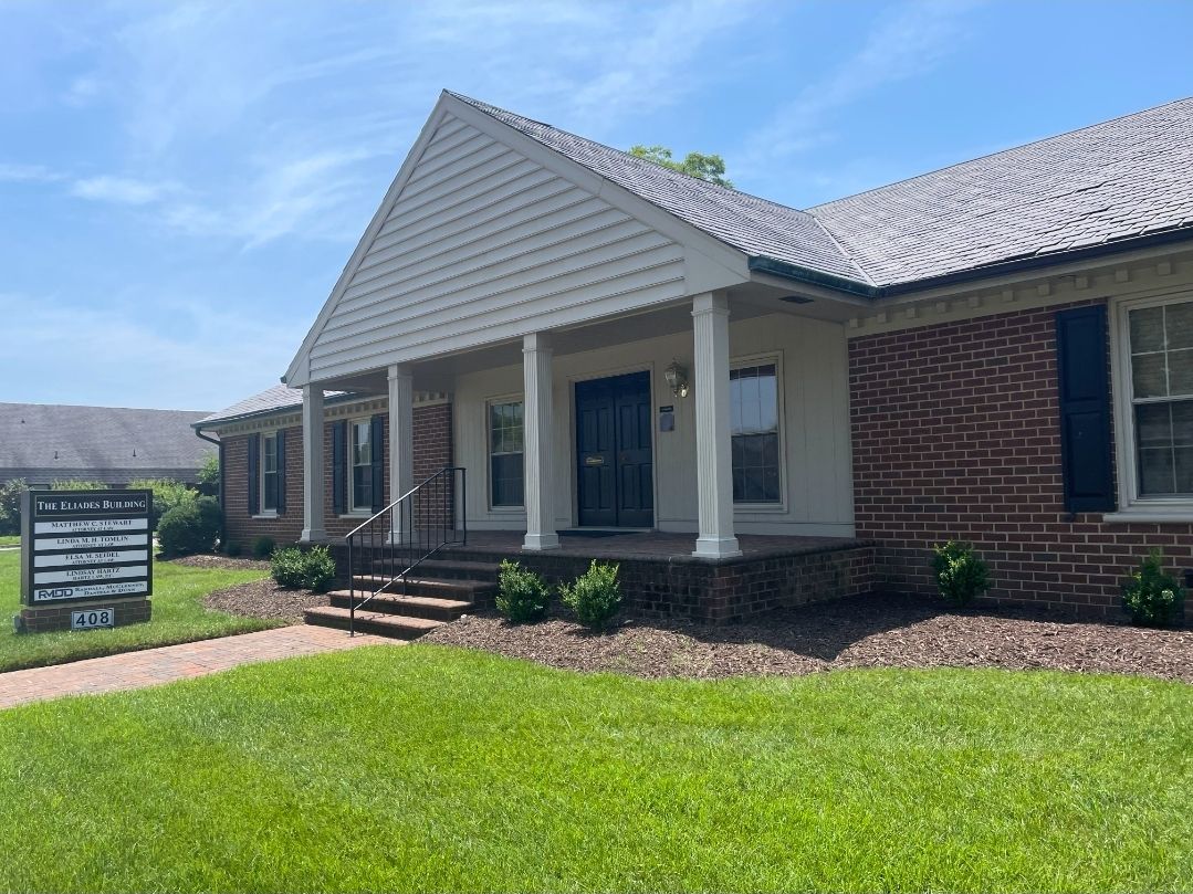 Single-story brick office building with white columns and front lawn on a sunny day.