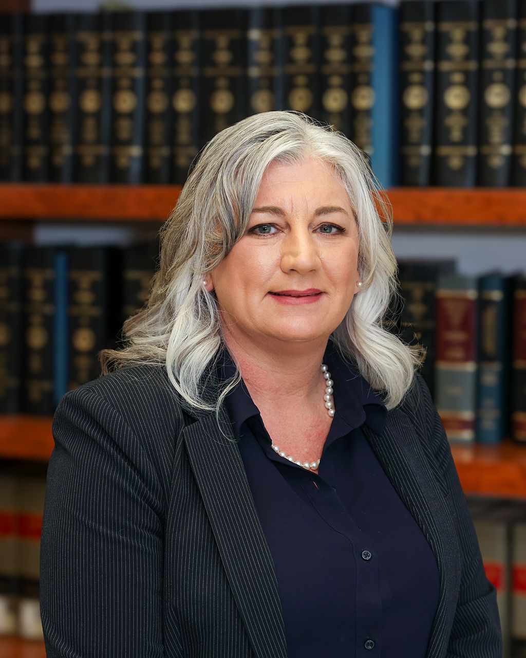 Tammy McClenney in a suit poses confidently in a library with legal books. Business, expertise, and elegance.