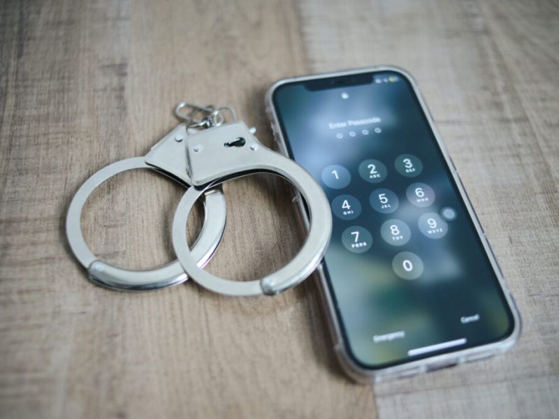 image of phone showing security password on screen and handcuffs on wooden background.