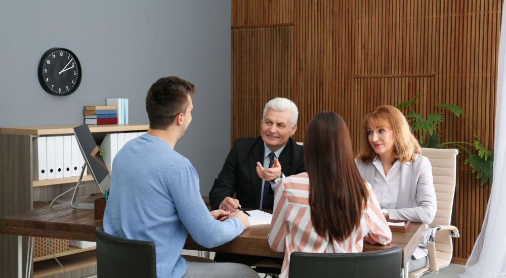 Business meeting with four people discussing in an office, using a laptop and documents on a wooden table.