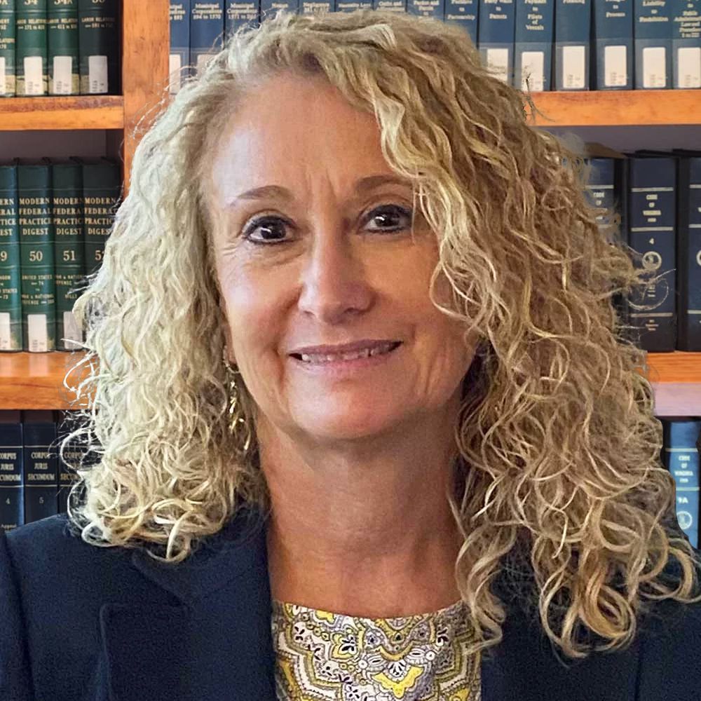 Portrait of a smiling woman with curly hair in front of bookshelves.