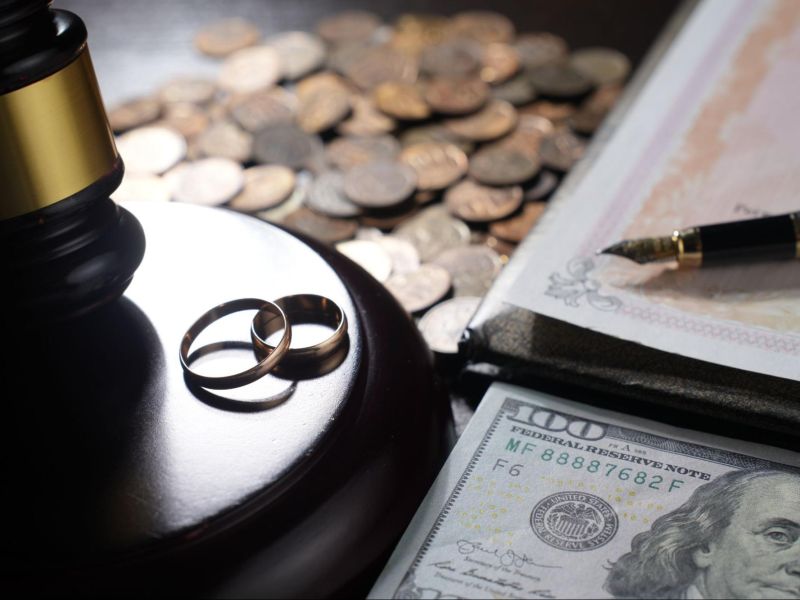 Wedding rings, gavel, currency, and documents symbolize divorce and financial settlement.