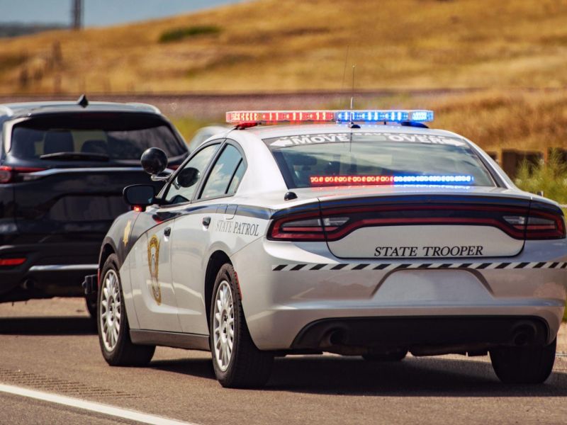 State trooper car with flashing lights pulls over a dark SUV on a rural road. Emergency response and law enforcement.