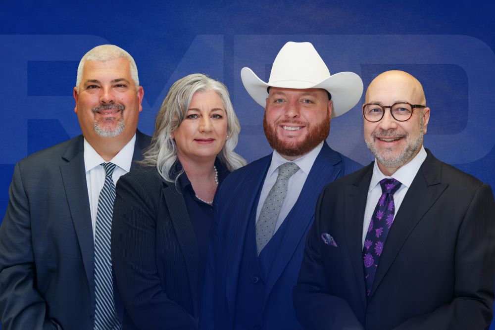 Two men and a woman in professional suits, including one wearing a white cowboy hat, pose against a blue background.