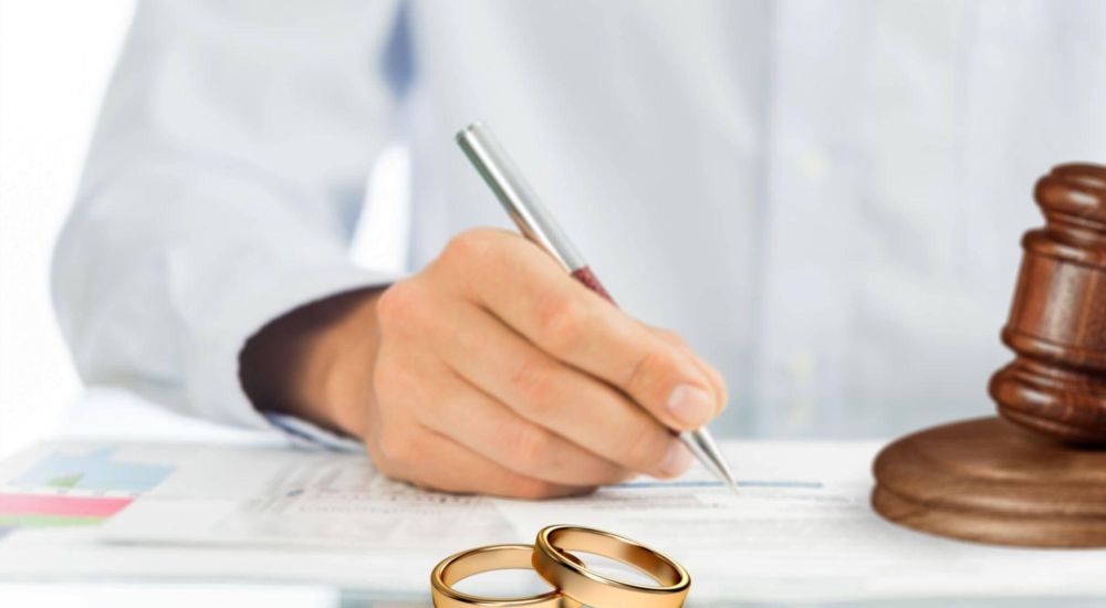 a person writing on a piece of paper with two wedding rings next to them