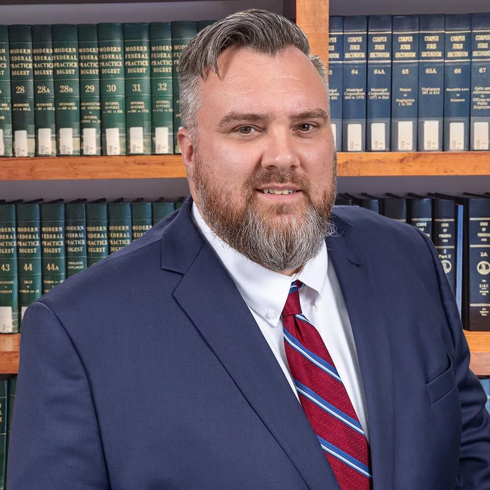 A man in a suit in front of bookshelves filled with legal texts, smiling confidently, representing professionalism and expertise.