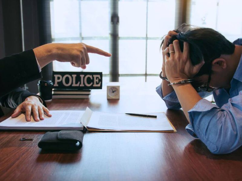 man with his head in his hands as police point at him across the table