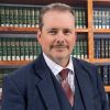 Professional man in a suit and tie standing in front of a bookshelf filled with legal books.