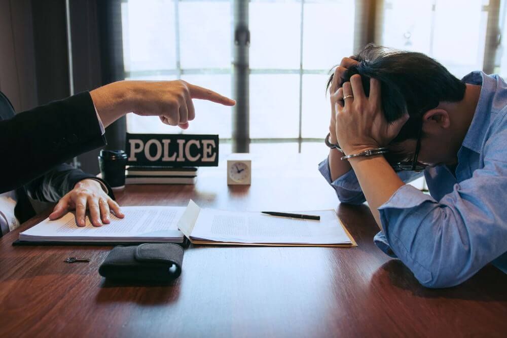 man with his head in his hands as police point at him across the table