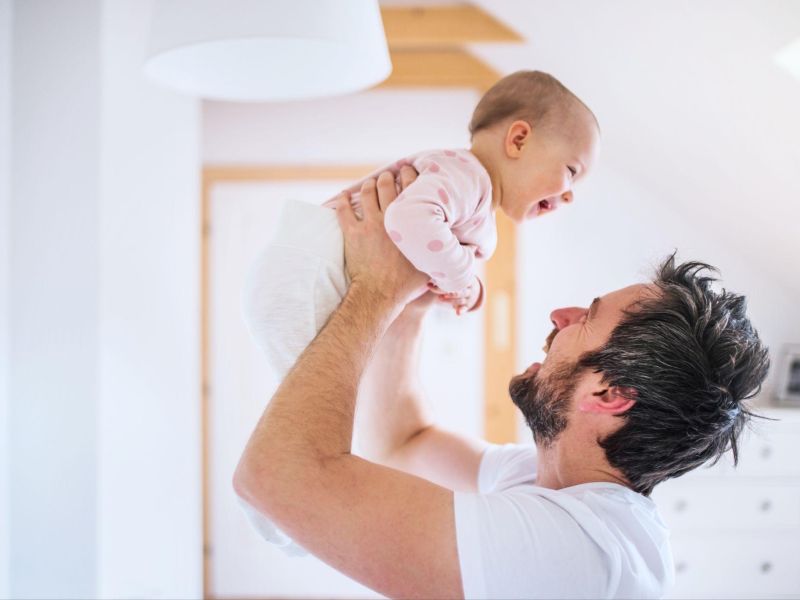 Father joyfully lifting smiling baby in bright room, showcasing parent-child bonding and happiness.