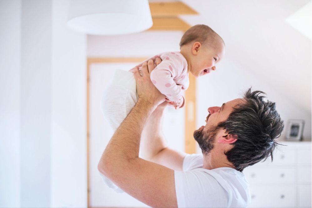 Father joyfully lifting smiling baby in bright room, showcasing parent-child bonding and happiness.