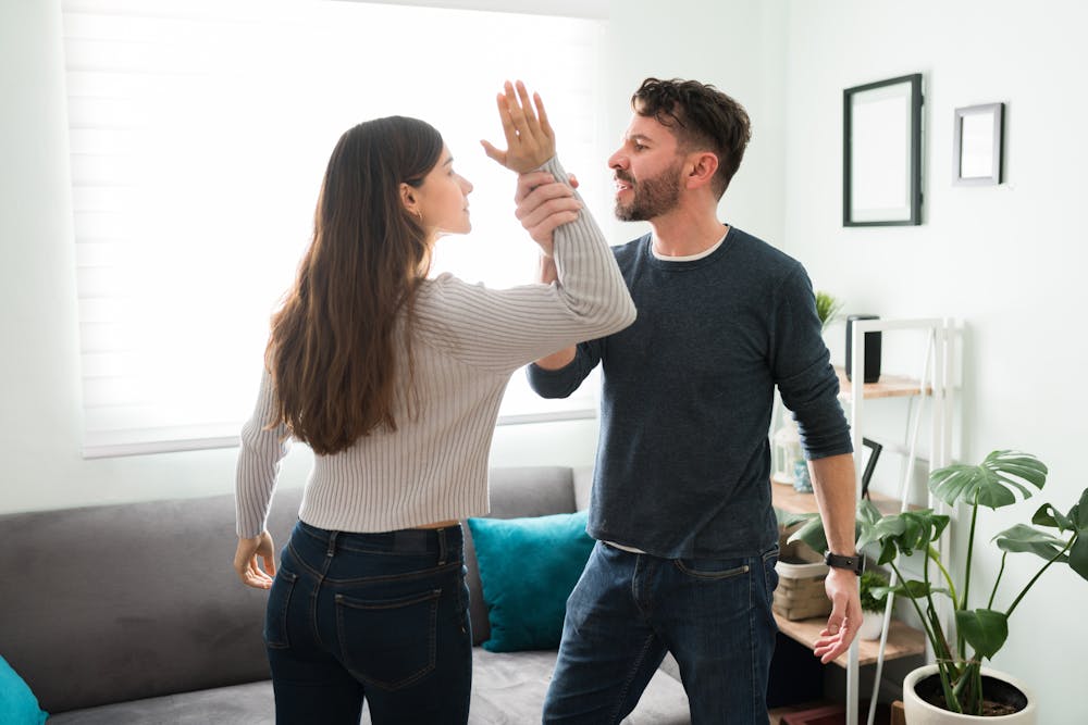 man grabbing the arm of a woman in living room to represent the dangers of domestic violence