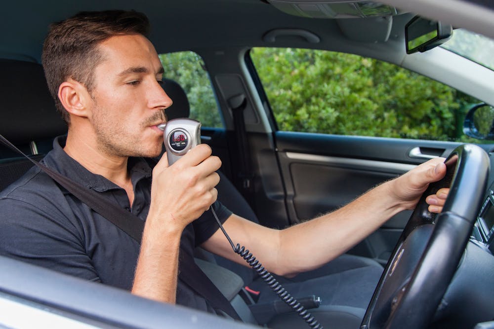 man blowing into a breathalyzer that's connected to his car