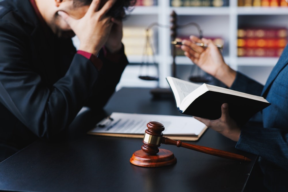 Lawyer consulting stressed client, open book and gavel on table in law office.