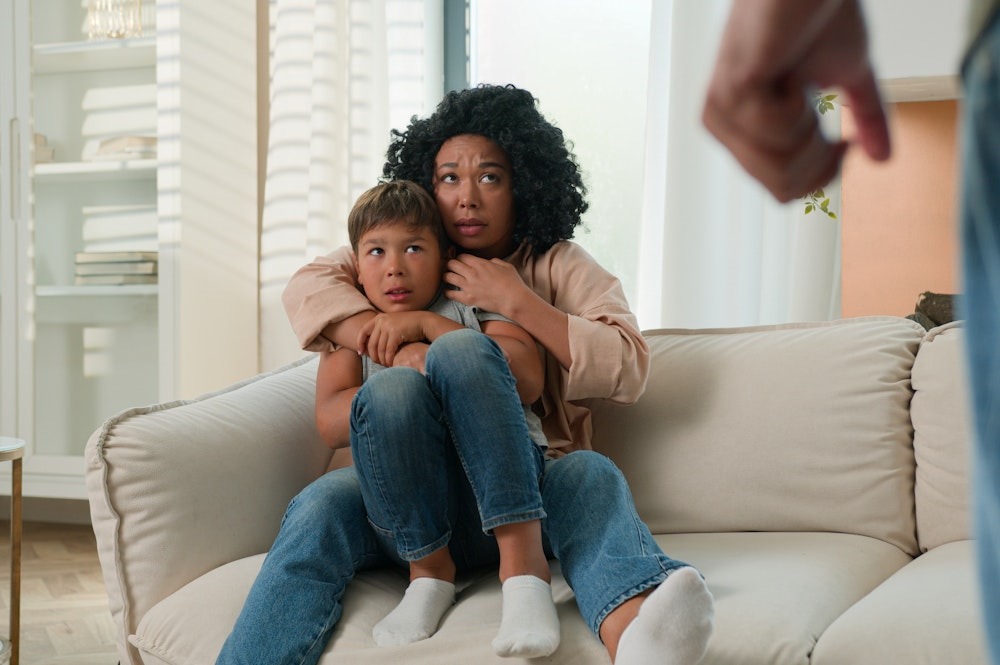 Mother and son on couch, looking anxious, with another person partially visible, creating a tense atmosphere.
