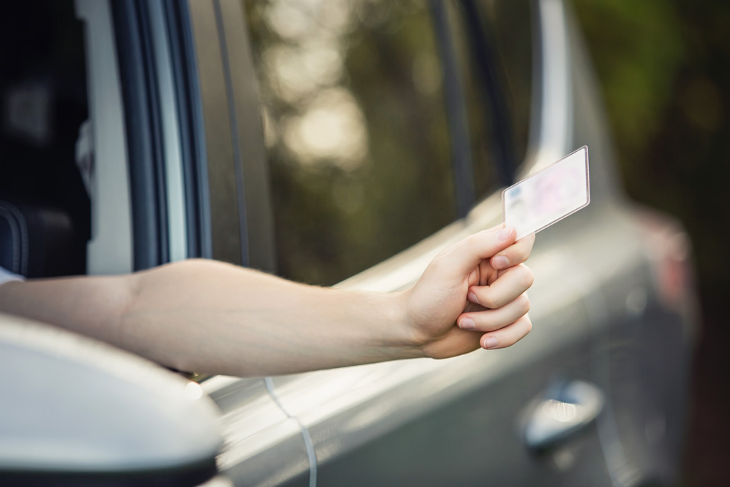 Hand holding a card through car window, focusing on transportation and identification.