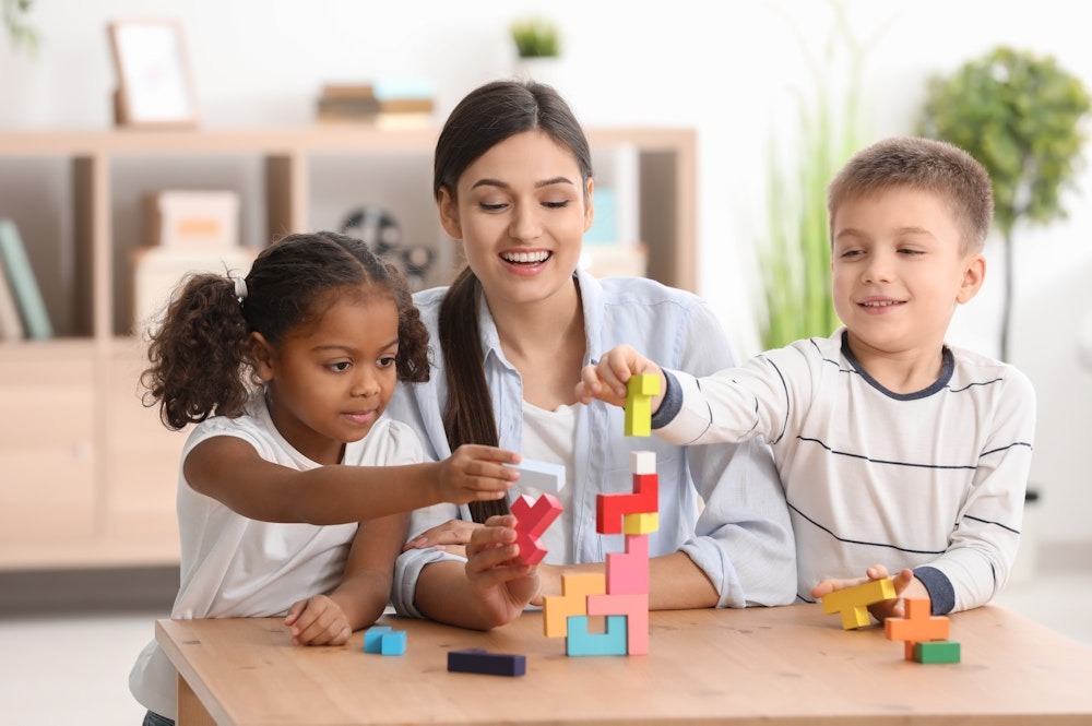Children and teacher playing with colorful building blocks, enhancing creativity and learning in a classroom setting.