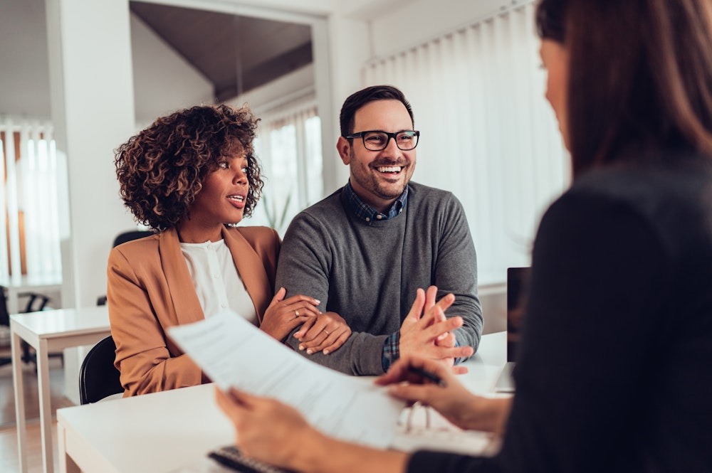Couple meeting for financial consultation in an office setting, smiling and engaged with a consultant holding documents.