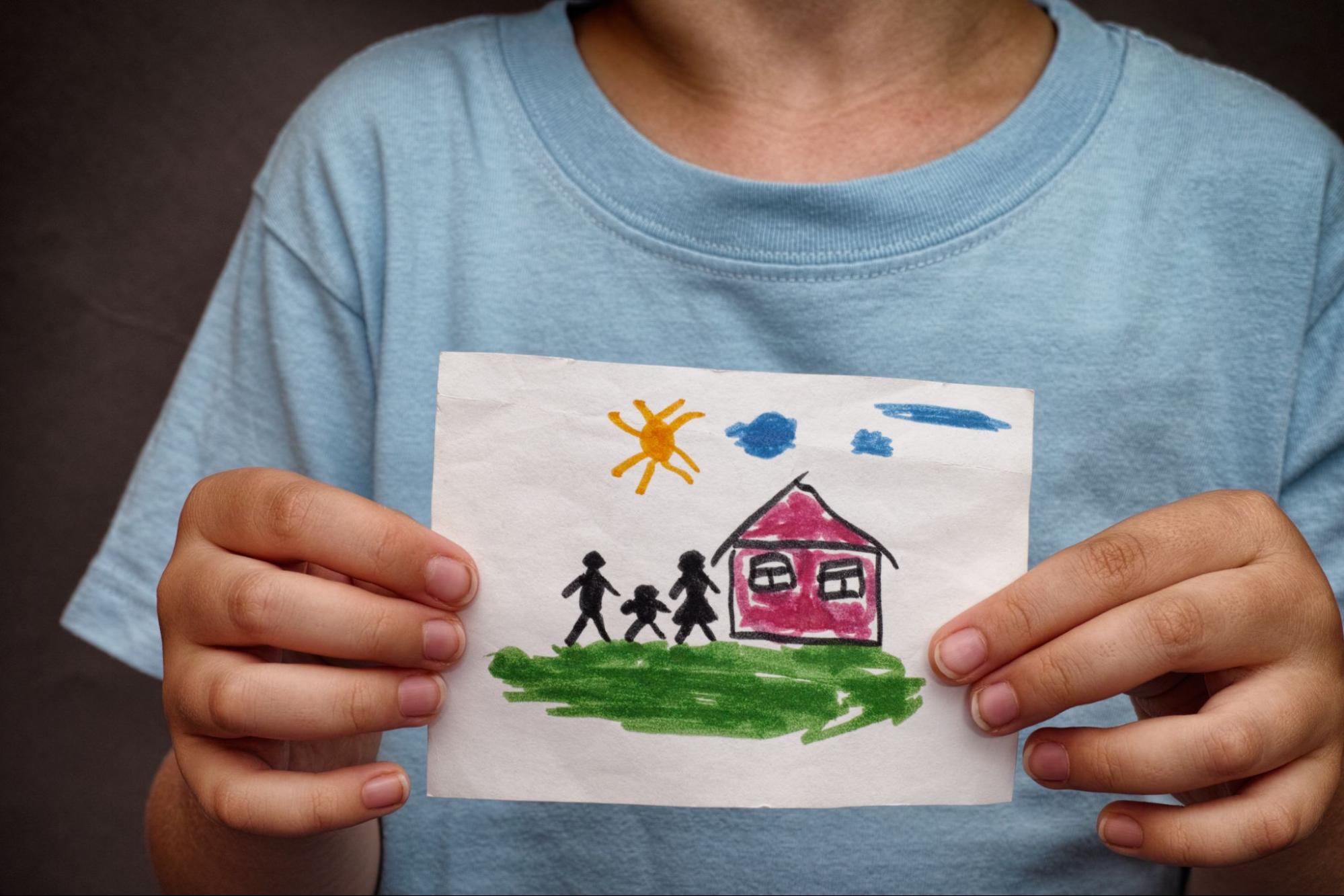 Child holding a drawing of a family, house, and sun, expressing joy and creativity in vibrant colors.
