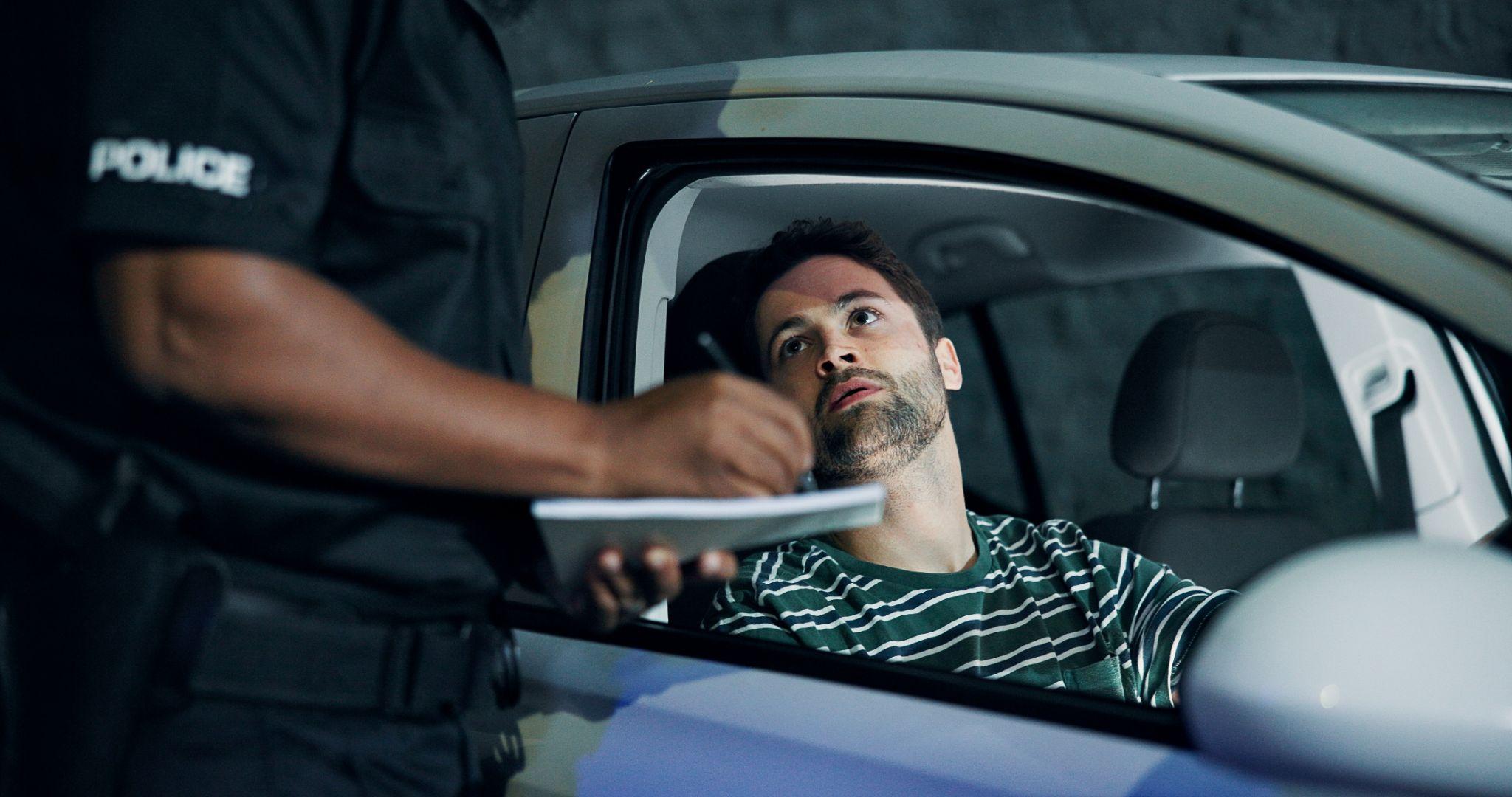 Officer writing a ticket for a seated driver during a traffic stop at night.