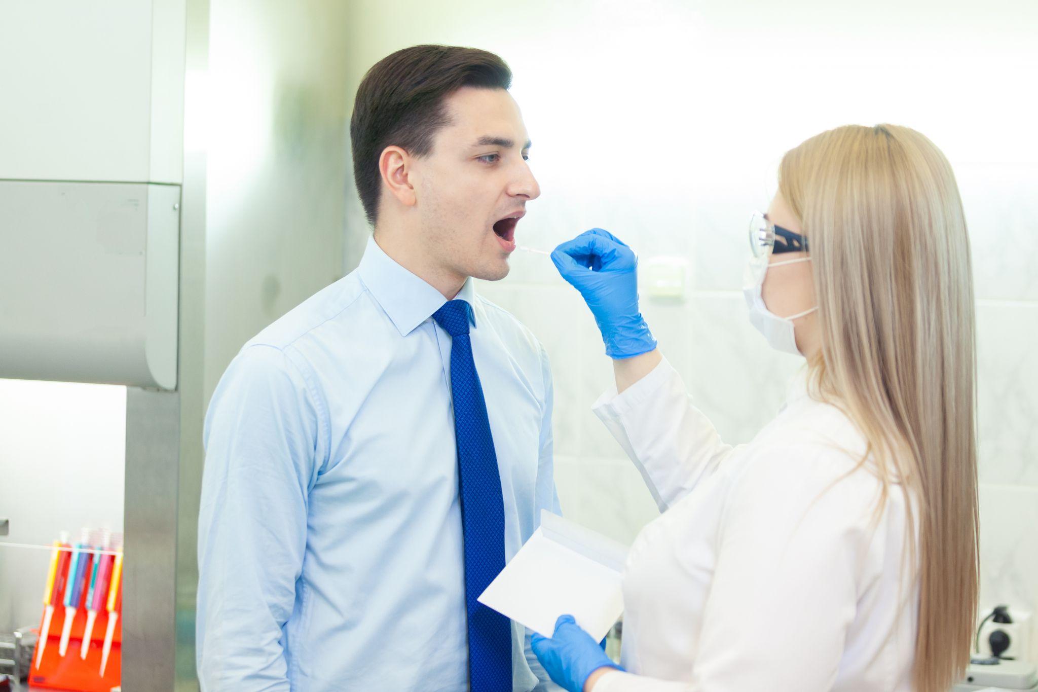 Healthcare professional taking a mouth swab sample from a man in a clinical setting.